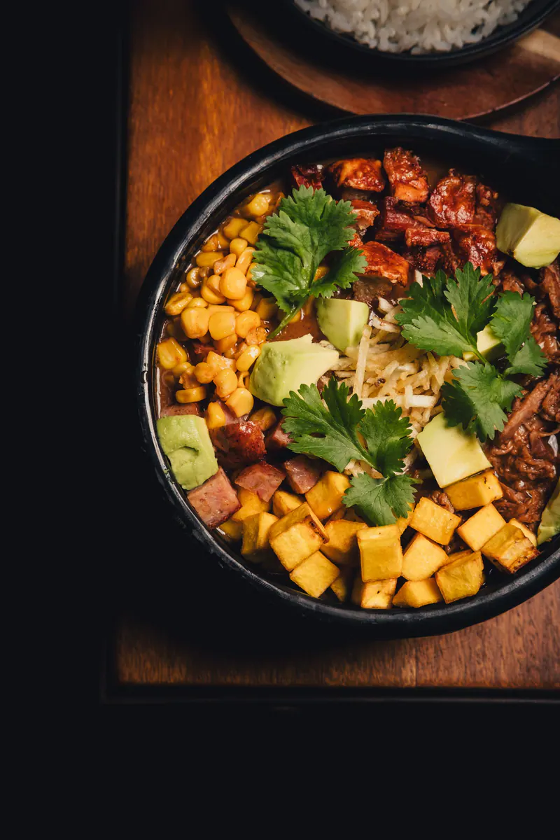 Cazuela de frijoles con chicharrón, aguacate, maíz y maduro, vista desde arriba