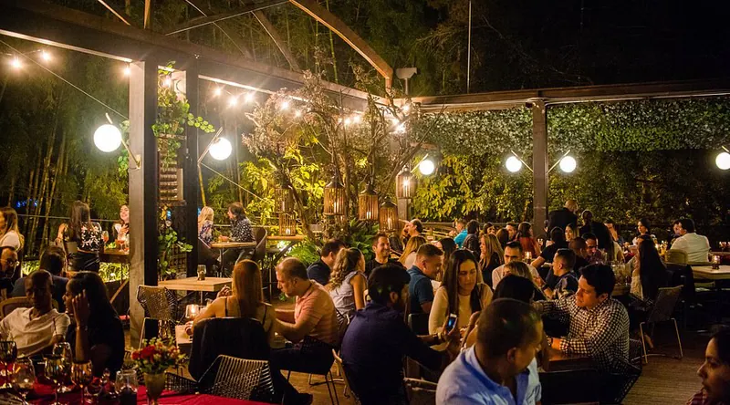 Bastardo Provenza's front garden at night: busy tables under pergolas with string lights and plants